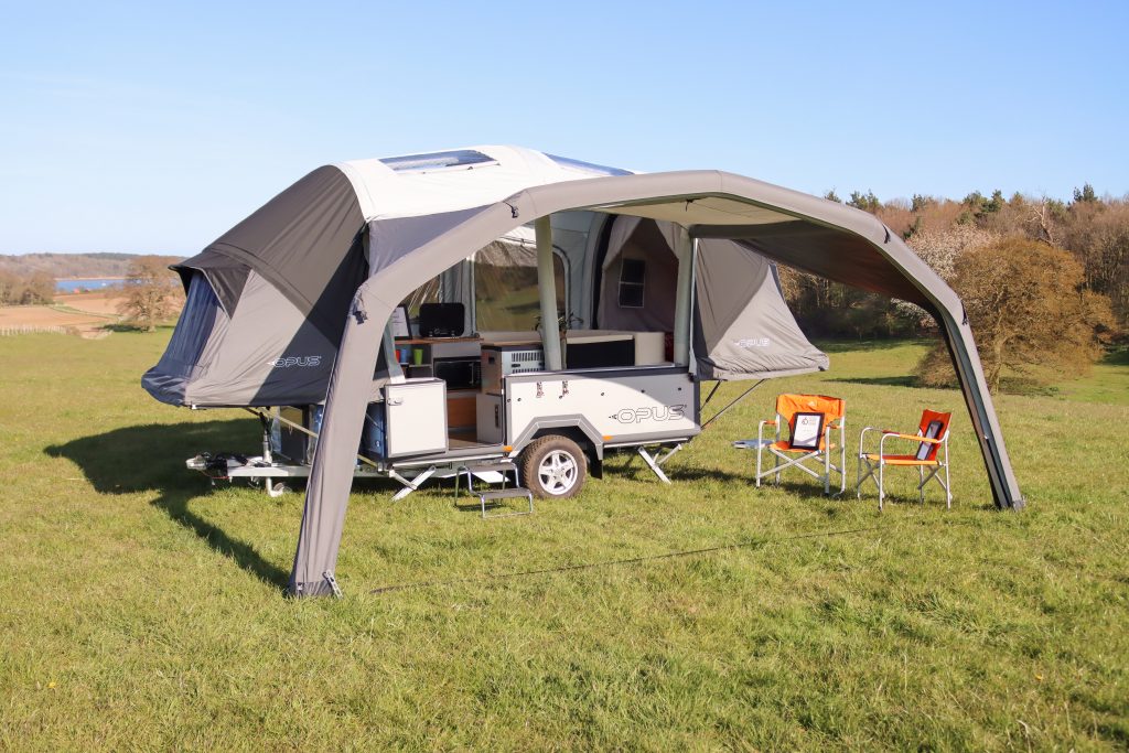 OPUS® Faltcamper auf einer Wiese. Mit Sonnensegel und Klappstühlen.