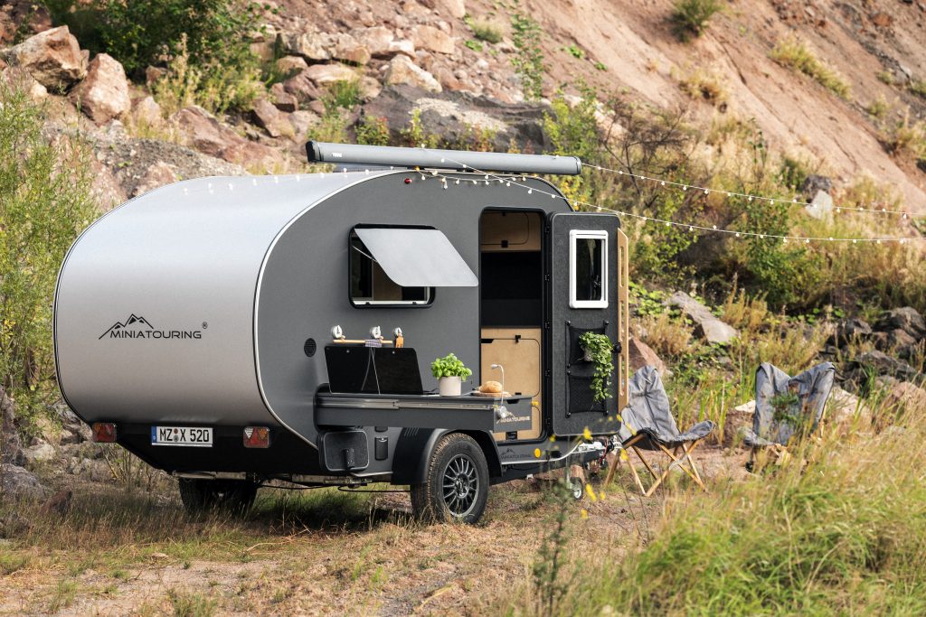 OPUS® Faltcamper auf einer Wiese. Mit Sonnensegel und Klappstühlen.