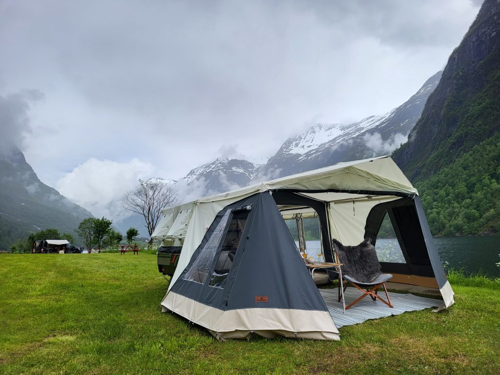 Combi-Camp Country Faltcaravan aufgebaut auf einer Wiese mit Bergen im Hintergrund.
